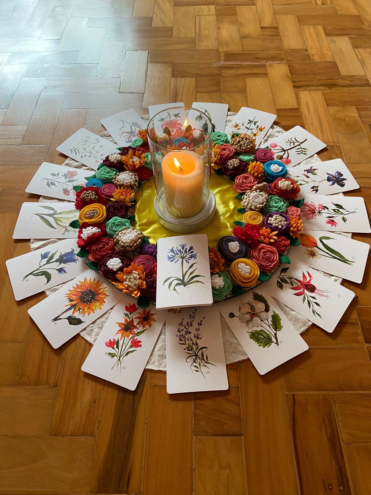 Centro da roda: vela acesa entre flores de feltro e cartas botânicas