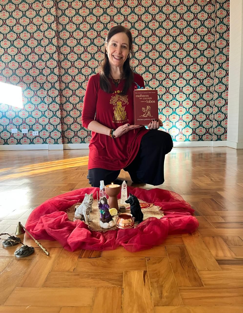Estela Gomes ajoelhada segurando o livro Mulheres que Correm com os Lobos, diante do centro da roda