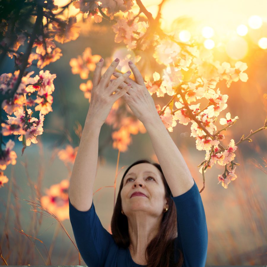 Estela Gomes com os braços erguidos entre flores, ao pôr do sol