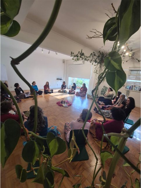 Círculo de mulheres sentadas, visto entre as folhas de uma planta